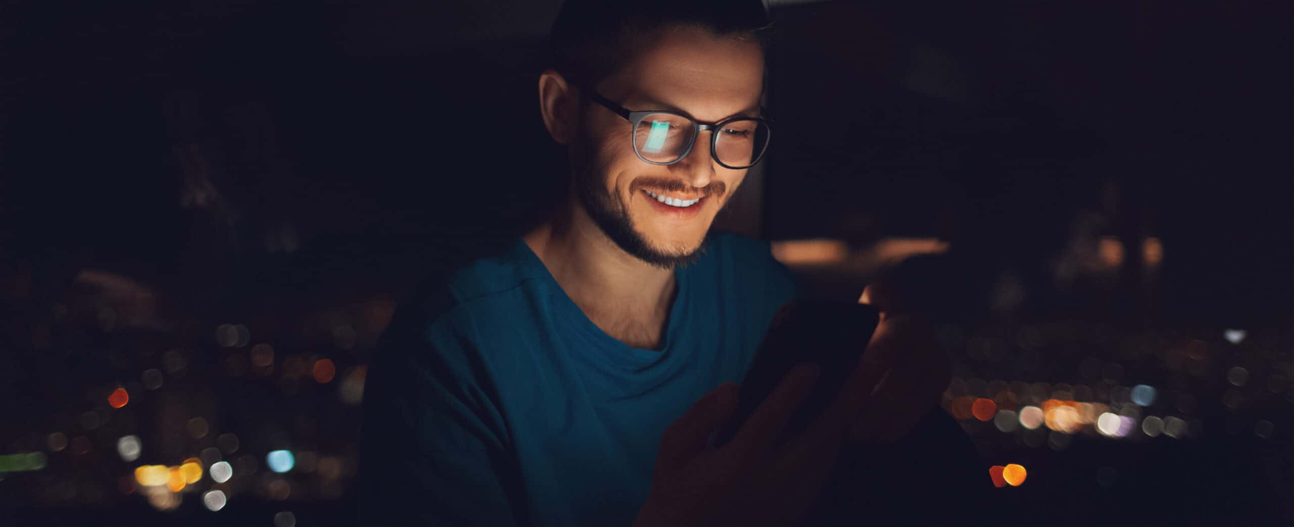 Night portrait of smiling man using smartphone near window