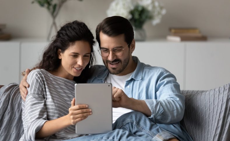 Couple sit on sofa using digital tablet buying on internet